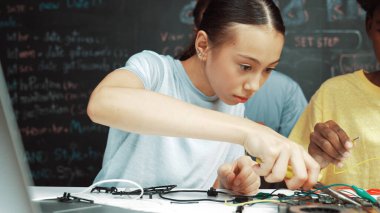 Kafkas öğretmeni STEM teknoloji sınıfında robot araba hazırlarken elektronik alet tamir tahtası kullanan mutlu lise öğrencisi. Tel ve anakart kullanarak çalışan çekici bir kız. Öğretim.