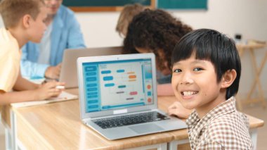 Energetic asian boy coding program and looking at camera in STEM class while caucasian teacher and diverse friend drawing mind map together. Student learning generated AI and writing code. Pedagogy. clipart