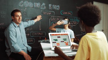 Akıl hocası karatahtayı işaret ederken ve mühendislik kodunu açıklarken VR gözlüğü takıyor. Afrikalı öğrenci yazma sistemi, öğretmenden elektronik aletlerle tavsiye alırken. Öğretim.