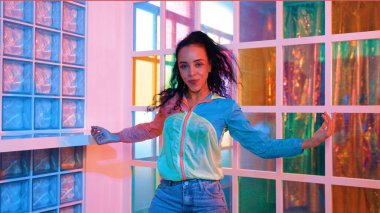 Neşeli İspanyol kız gece kulübünde renkli giysiler giyerken neon ışıkta müzik eşliğinde hareket ediyor. Sokak dansçısı kameraya bakarken hareketli adımlar atıyor. Mutluluk.