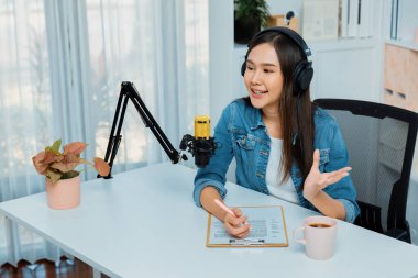 Sosyal medyada kulaklıkla canlı yayın yapan Asyalı sunucu modern stüdyoda yaşam koçluğu veya pazarlama dinleyicilerini selamlıyor. Taktik.