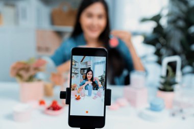 Seçici odak akıllı telefonu ile genç ve güzel Asyalı makyaj fırçası yanak testi koleksiyonunu pastel renkli, sosyal medyada tanıtım yapmak için ışıldayan bir ruh hali gösteriyor. Taktik.