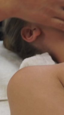 Lüks bir spa merkezinde masaj terapisti tarafından yüz masajı ve spa tedavisi için kaplıcaya uzanmış rahat bir kadın. Sağlık, stres atma ve gençleştirme kavramı.