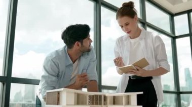 Beyaz mimar mühendis takımı ev modelini ölçmek için birlikte çalışıyor. Genç, güzel tasarımcı ev inşaatı yazarken erkek işçiler mimari modelleri inceliyor, inceliyor, inceliyor. Tartışma