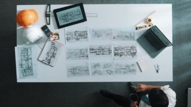 Proje planını kontrol ederken ve seçerken mimar mühendisin bina planlarını masaya yerleştirdiği tepeden aşağı hava görüntüsü. İç mimar toplantı masasından mimari plan seçti. Hizalama.