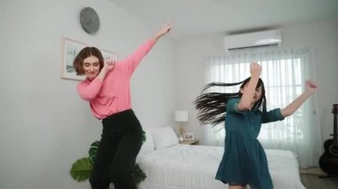 Yatak odasında Asyalı kızıyla müzik eşliğinde dans eden mutlu çekici anne. Beyaz anne dans eder ya da egzersiz yapar. Bu arada tatlı çocuk da müzik eşliğinde yatağa atlar. Aile eğlence konsepti. Pedagoji.