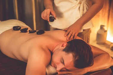 Sıcak mum ışığıyla lüks bir tatil köyündeki kaplıca salonunda sıcak taş masajı, mutlu erkek müşteri bazalt taşı masajının keyfini çıkarırken rahatlatıcı bir sıcaklıkla vücudun üzerinde süzülüyor. Sessiz.