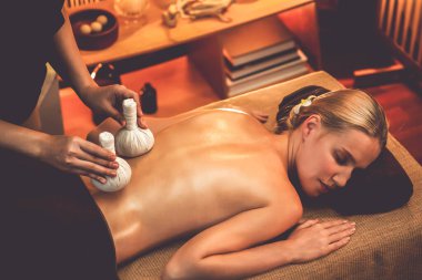 Sıcak bitkisel top spa masaj vücut tedavisi, masör kadın vücuduna nazikçe şifalı bitki torbası bastırıyor. Aromaterapi tesisinin sakinliği ve dinginliği kaplıca salonundaki mumların sıcacık ışığında. Sessiz.