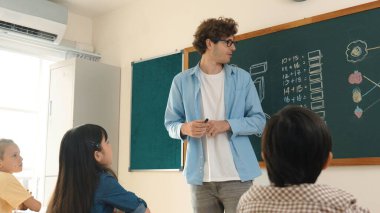 Matematik formülü veya teorisi ile karatahtanın önünde dururken sınıfın etrafına bakan profesyonel akıl hocası. Çeşitli ilköğretim öğrencileri matematik dersinde öğreniyor, çalışıyor ve oturuyor. Pedagoji.