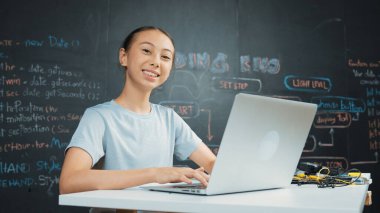 Kara tahtada dizüstü bilgisayar kullanarak akıllı kız programlama sistemi. Lise öğrencisi mühendislik kodları yazıyor ya da STEM teknoloji sınıfında kameraya bakarken bir şey söylüyor. Yaratıcı eğitim. Öğretim.