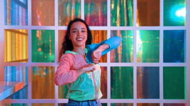 Neşeli İspanyol kız gece kulübünde renkli giysiler giyerken neon ışıkta müzik eşliğinde hareket ediyor. Sokak dansçısı kameraya bakarken hareketli adımlar atıyor. Mutluluk.