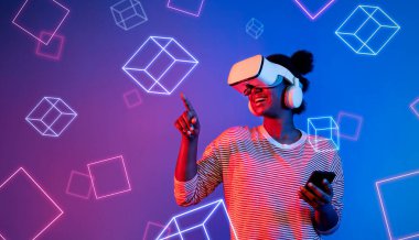 VR gözlüklü Afrikalı kız mavi ve pembe arka planda duruyor ve yüzen geometrik şekle bakıyor. Heyecanlı insan görsel gerçeklik dünyasına giriyor. Teknoloji yeniliği. Yaratıcılık.