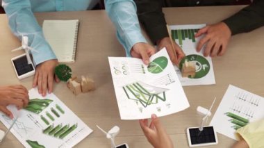 Eko evi projesini yel değirmeni tasarım modeli ve karbon ayak izini azaltmak için yeşil enerji kullanım grafiği ile toplantı masasında tartışan harika bir iş ekibi. Dünyayı kurtarın. Eline odaklan. Tanımlama.