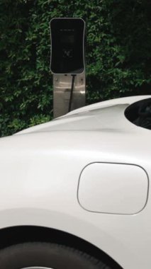 İlerici adam elektrikli aracına elektrik kablosu takıyor. Ev şarj istasyonundan EV arabası. Çevreyi korumak için temiz ve yenilenebilir enerji kullanan elektrikli bir araba. Çevre dostu otomobil.