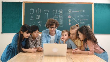 Kafkas öğretmeni ve çeşitli öğrenciler sınıfta dizüstü bilgisayara bakıyor. Kodlama programını öğrenen ya da öğretmenlik yaparken yazılım kullanarak oluşturulan çok kültürlü çocuklar. Pedagoji.