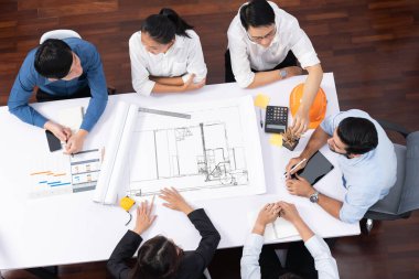 Mimari proje üzerinde birlikte çalışan, inşaat planını gözden geçiren ve toplantı masasında plan oluşturan çeşitli inşaat mühendisi ve müşteri gruplarından oluşan üst düzey bir pankart. Tedbirli