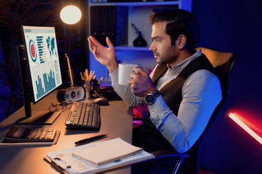 Gülümseyen zeki işadamı, elinde kahve fincanı olan satış ekibiyle buluşuyor ve geceleri Mor Neon Light Home Office 'deki bilgisayar ekranında ürün hedef pazarını araştırıyor. Tahmin et..