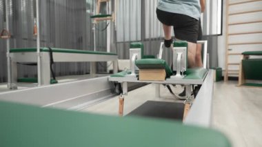 Esneklik ve dayanıklılığı artırmak için pilates reformcusu üzerinde diz çökme alıştırması yapan bir adam. Antrenör asistanı dengeyi arttırmak için yenilikçiye hamle yapıyor. Alışkanlık.