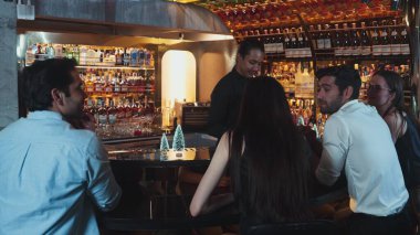 Gülümseyen Asyalı barmen VIP konuğuyla konuşurken süslü Noel ağacı tezgahında karışık kokteyl hazırlıyor. Gece kulübü lüksünde gece hayatını gösteren özel bir içecek. Vinosity.