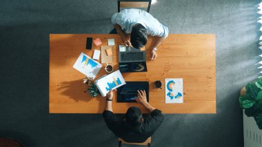 Erkek lider, pazarlama ekibi tablet üzerinde çalışırken ve mali tablolara bakarken grafiği analiz etmek için dizüstü bilgisayar kullanıyor. Başlangıç grubunun çözüm bulma ve birlikte plan yapma stratejisinin en üst görünümü. Cemaat.