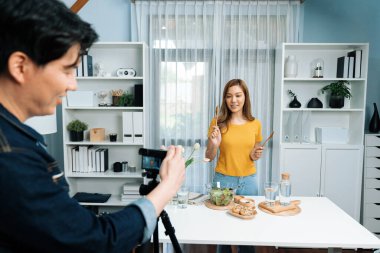 Asyalı güzel kadın yemek uzmanı blog yazarı akıllı kameramanın sosyal medya kavramında canlı yayında kaydettiği canlı yayında salatanın nasıl kolay pişirileceğini öğretiyor. İnfobahn.