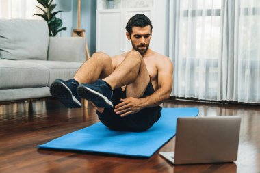 Atletik ve sporcu adam spor paspası üzerinde çatırdarken evdeki formda fiziğe ve sağlıklı spor yaşam tarzına uygun online ev eğitimi takip ediyor. Çevrimiçi neşeli ev egzersizi videosu.