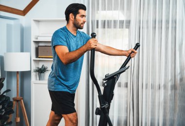 Evdeki formda fizik ve sağlıklı spor yaşam tarzı için vücut egzersizi sırasında eliptik koşu makinesiyle koşan atletik ve sportif bir adam. Gaiety evde egzersiz eğitimi.
