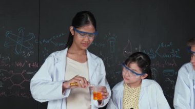 Değişik öğrenciler masada mikroskop ya da tüpü sıvıyla karıştırırken renkli solüsyonları karıştırıyorlar. Kimyasal teorisiyle karatahtanın önünde duran Asyalı kız deney tüpü tutuyor. Öğretim