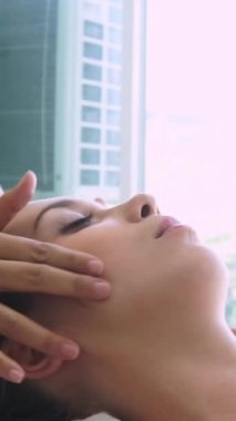 Lüks bir spa merkezinde masaj terapisti tarafından yüz masajı ve spa tedavisi için kaplıcaya uzanmış rahat bir kadın. Sağlık, stres atma ve gençleştirme kavramı.