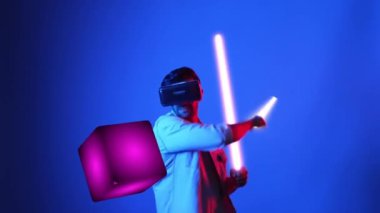 Parlayan kılıcı tutan ve VR gözlük takan oyuncu oyun oynuyor. Çekici erkek model sanal gerçeklik gözlüğü kullanarak yüzen bloğu eskrirken heyecanlanıyor. Teknoloji yeniliği. Aygıt.