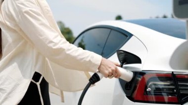 Ağır çekimde çalışan kadın şarj aletini şarj istasyonundan elektrikli araba aküsünü şarj etmek için kullandı. Sürdürülebilir çevre dostu seyahat konsepti için alternatif enerji ve şarj edilebilir EV araba. Yararlı
