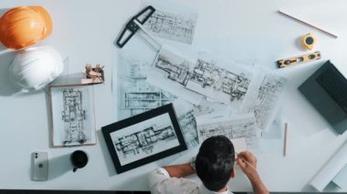İnşaat mühendisi inşaatı planlarken ve proje planı ve dizüstü bilgisayarla toplantı masasında otururken planlara bakarken tepeden tırnağa. Mimar bina tasarımı hakkında not alıyor. Hizalama.