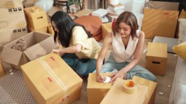 Çekici bir oda arkadaşı oturma odasında paket paketlerken pakette konum yazıyor. Mutlu satıcı birlikte çalışıyor ve teslimat paketini hazırlıyor. Girişimci kargo kutusu paketliyor. Myrmidon.