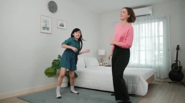 Yatak odasında Asyalı kızıyla müzik eşliğinde dans eden mutlu çekici anne. Beyaz anne dans eder ya da egzersiz yapar. Bu arada tatlı çocuk da müzik eşliğinde yatağa atlar. Aile eğlence konsepti. Pedagoji.