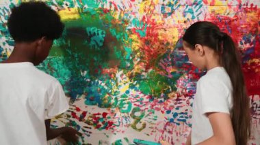 Genç ve çeşitli çocukların arka görünüşleri renkli duvarları elle boyarlar. Çekici bir lise öğrencisi renk paletini tutarken duvarı el iziyle boyuyor. Yaratıcı aktivite. Öğretim