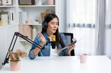 Sosyal medyada kulaklıkla canlı yayın yapan Asyalı sunucu modern stüdyoda yaşam koçluğu veya pazarlama dinleyicilerini selamlıyor. Taktik.