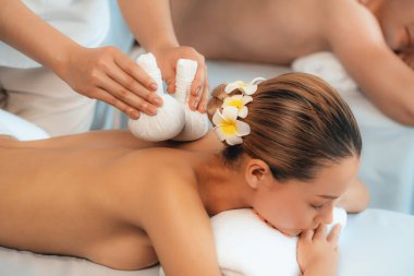 Sıcak bitkisel top spa masaj vücut tedavisi, masör nazikçe bitki torbasını çift müşteri vücuduna bastırıyor. Aromaterapi dinlenme sükuneti ve sükuneti kaplıca salonundaki atmosferi aydınlatıyor. Sessiz.