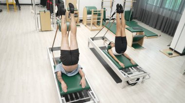 Müşteri, spor salonundaki yenilikçi bir makinede kayışla ters bacak kaldırma hareketi yapıyor. Çekirdek bağlantısını, dengesini ve esnekliğini geliştirmek için ters takla atan iki mutlu antrenör. Alışkanlık.