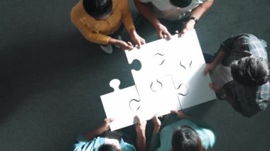 İş dünyasına yukarıdan bakan insanlar bulmacayı tamamlamak için yapbozun son parçalarını bir araya getiriyorlar ve günlük giysiler giyerek ayakta duruyorlar. Çeşitli takımlar takım çalışması ile çözüm buluyor. Sempozyum.