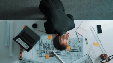 Yetenekli proje yöneticisinin proje planının zaman aşımına uğraması ve toplantı masasında bulunan mimar mühendise ekipman, cetvel, güvenlik kaskı ve dizüstü bilgisayar dağınıklığı ile ev tasarımını açıklamak. Hizalama.