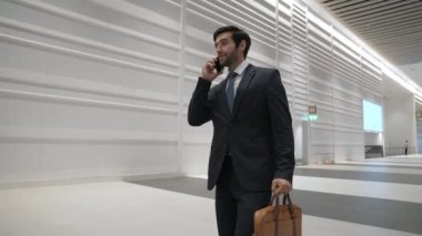 Profesyonel lider, işe başlama projesi için iş ekibini ararken ofise doğru yürüyor. Yakışıklı erkek lider toplantı odasına giderken telefonla pazarlama planı hakkında rapor veriyor. Sevinçli..