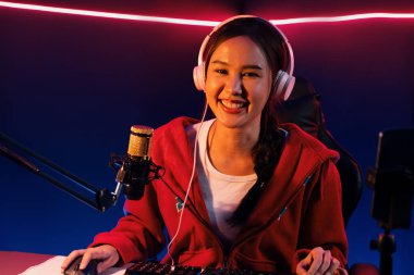 İnternet üzerinden kulaklık takıp gülümseyen Asyalı güzel kız flamasının sunucu kanalı izleyicilerle internet üzerinden konuşma yapıyor. Esport yetenekli takım oyuncuları neon mavi odada. Taktik.