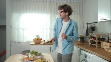 Mutlu baba yemek pişirirken müziğe geçiyor ve modern mutfakta öğle yemeği hazırlıyor. Aktif baba, sebze ve mutfak gereçleri ile çevrili sağlıklı yemek ya da salata yaparken şarkıyla dans ediyor. Pedagoji.