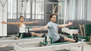 Pilates reformatör makinelerinde senkronize kol uzantıları yapan iki müşteri. Mutlu pilates partnerleri, esnekliği arttırmak ve dengeyi ve kontrolü sağlamak için reformcunun üzerine oturdular. Alışkanlık.