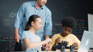 Kafkas öğretmen dizüstü bilgisayara bakarken araba modelleme sistemini kara tahtada kodlama veya programlama koduyla açıklıyor. Robot inşaatını öğrenen çeşitli öğrencileriniz kutlu olsun. Öğretim.