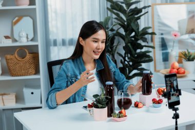 Gülümseyen, güzel Asyalı genç, lezzetli karışık çilek ve kiraz suyu detoksu içeceklerini inceleyen, sosyal medyada özel promosyon satışı için sağlıklı ürünler sergileyen. Taktik.