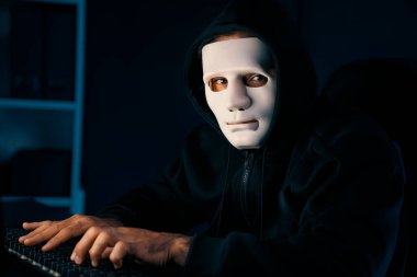 Beyaz suçlu anonim maske kameraya bakarken aynı zamanda bilgisayar başında sunucu sürücüsü sistemi olan mavi neon aydınlatma odasındaki klavyeye virüs şifrelemesi yerleştiriyor. Tahmin et..