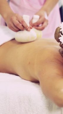 Masaj terapisti, lüks bir spa merkezindeki spa yatağında yatan bir kadını tedavi etmek için bitkisel kompres kullanıyor. Sağlık, stres atma ve gençleştirme kavramı.