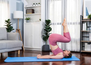 Spor kıyafetleri içinde esnek ve becerikli bir kadın evde egzersiz paspası üzerinde meditasyon pozisyonunda yoga yapıyor. Huzurlu ve huzurlu bir yoga yaşam tarzı..
