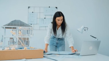 Genç, güzel beyaz bir mimar masanın üzerine plan koyar ve ev modeliyle karşılaştırırken, modern ofisteki fahişe modellerini dikkatlice incelerken arkadaki çizgilerle karşılaştırır. Tertemiz..